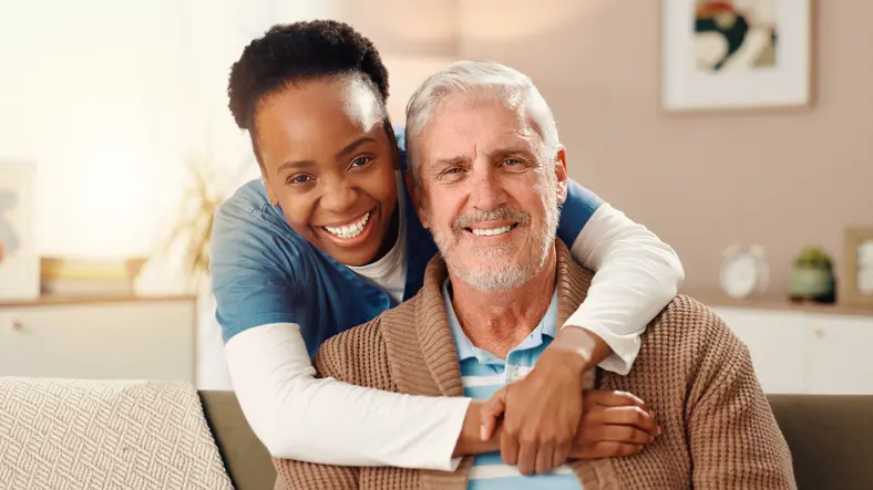 Smiling caregiver hugging elderly man warmly.
